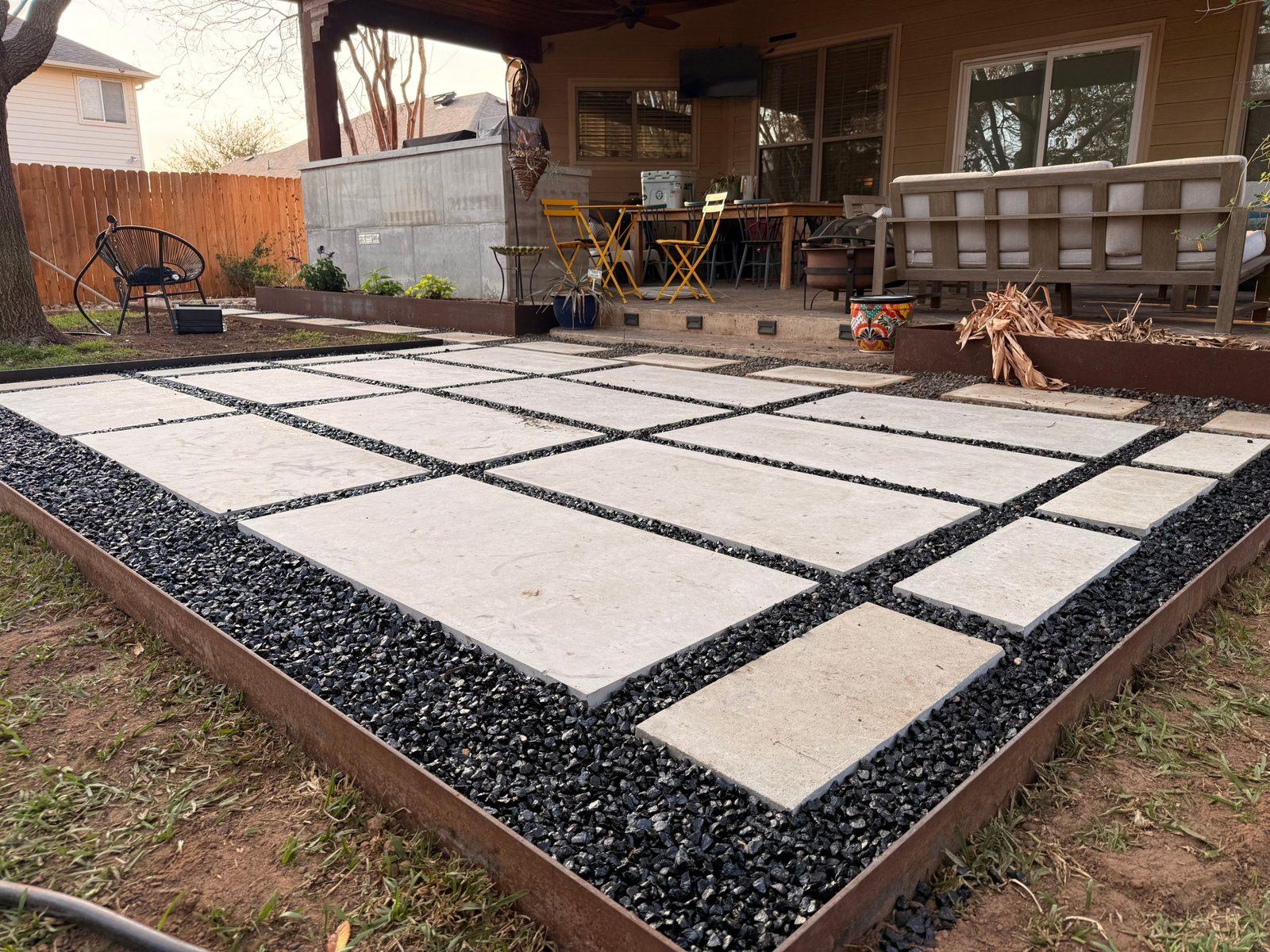 Large-format stone paver patio with black rock and steel edging, installed by A's Exterior Services